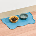 Blue bone-shaped raised-edge pet feeding mat holding a yellow food bowl and a grey water bowl.