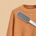 Blue double-sided pet hair brush resting on an orange knit sweater.